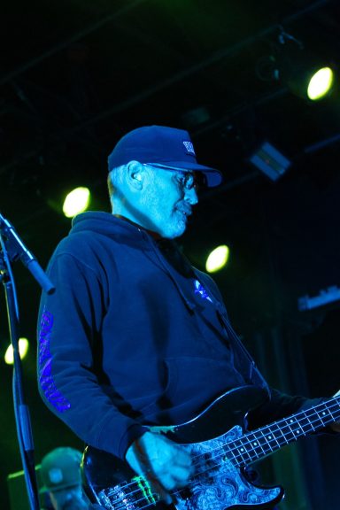A musician playing bass guitar on stage under blue and green lights.