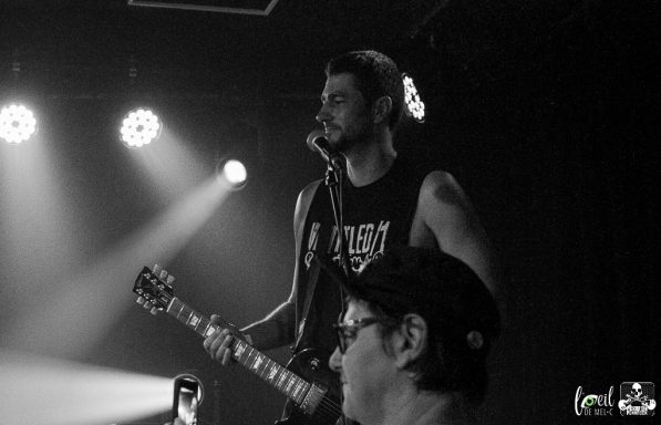 A musician performs on stage with a guitar while an audience member watches.