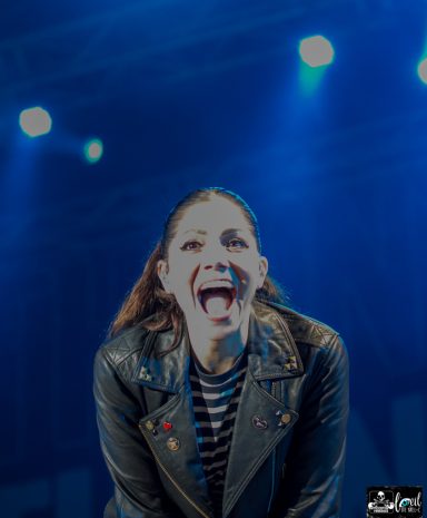 Person with a big smile wearing a leather jacket under blue stage lights.