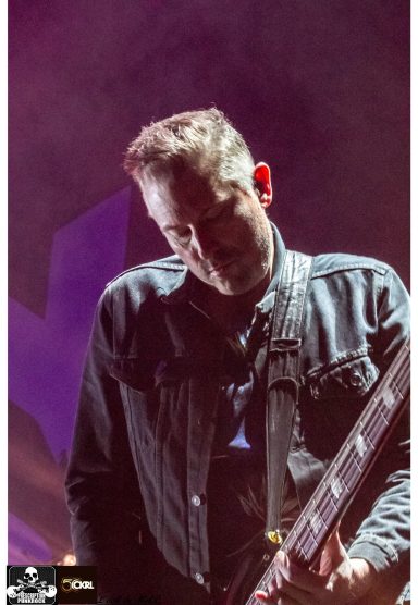 Musician playing guitar on stage, with focused expression and dramatic lighting.