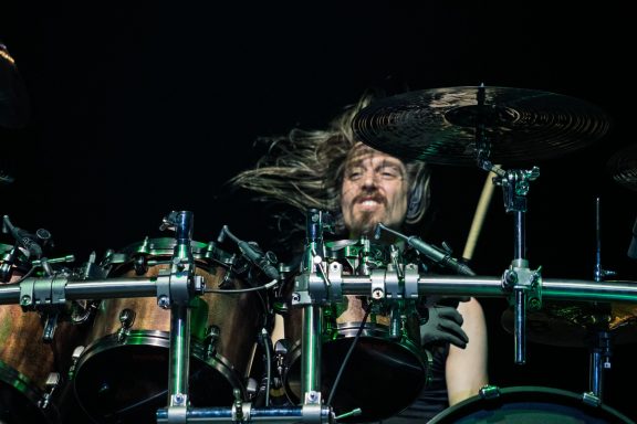 A drummer passionately performing on stage, with long hair flying and focused expression.