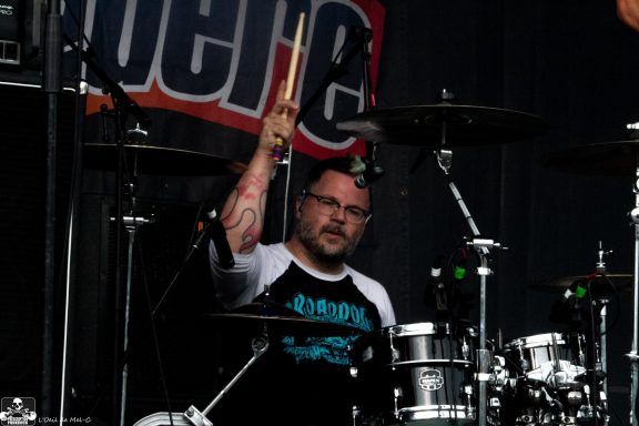 Drummer performing on stage with a focused expression and holding drumsticks.