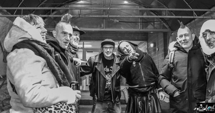 A group of six people with mohawks, smiling and posing together in a dimly lit setting.