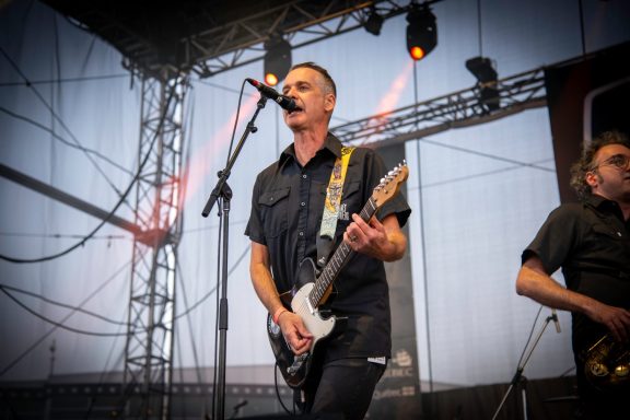 Musician performing on stage with a guitar, singing into a microphone.