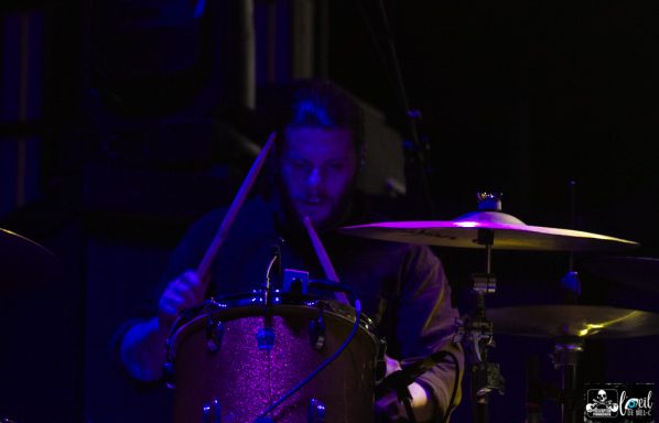 A drummer playing with focus under purple stage lights.
