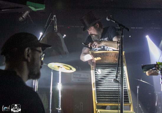 A musician plays a washboard on stage, illuminated by colorful lights.