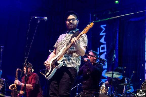 Musicians performing on stage with various instruments and a backdrop banner.