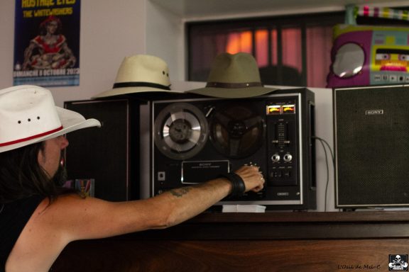 A person adjusting an old stereo with hats on top and colorful decor in the background.