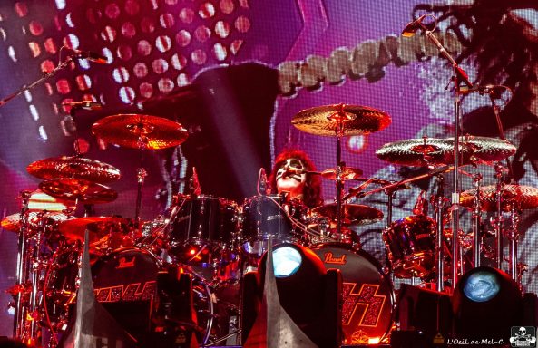 Drummer performing on stage, surrounded by vibrant lights and equipment.