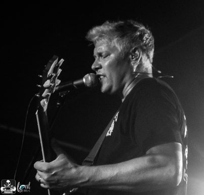 Black and white photo of a musician singing into a microphone while holding a guitar.