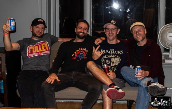 Four friends sitting on a couch, each holding a beverage, smiling and posing for the camera.
