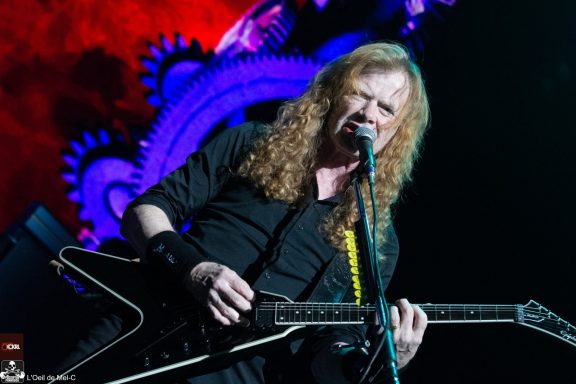 A musician with long hair performs passionately on stage with a guitar.