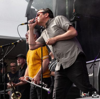 A musician sings passionately into a microphone while a trumpet player stands nearby.