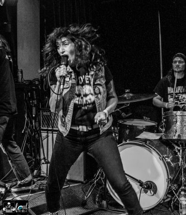 A female vocalist passionately performs on stage with a band in a lively concert setting.