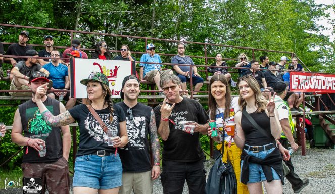 A diverse group of people posing outdoors at a lively event, with banners in the background.