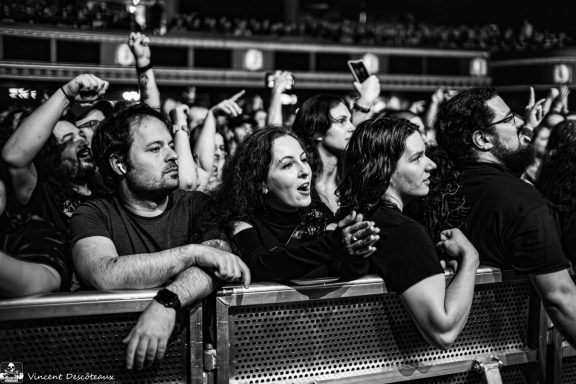 Crowd at a concert, showing enthusiastic fans with raised arms and intense expressions.