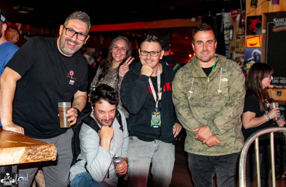 Group of five people posing together in a lively bar setting.