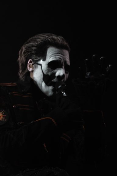 A performer with white face paint and black clothing, striking a dramatic pose.