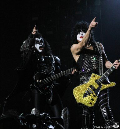 Two musicians in elaborate costumes perform on stage, one holding a guitar and pointing.