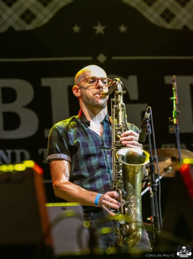 Musician playing saxophone on stage with a lively background.